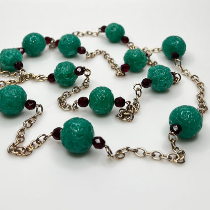 Close-up of textured green art glass beads with red faceted accents and gold chain