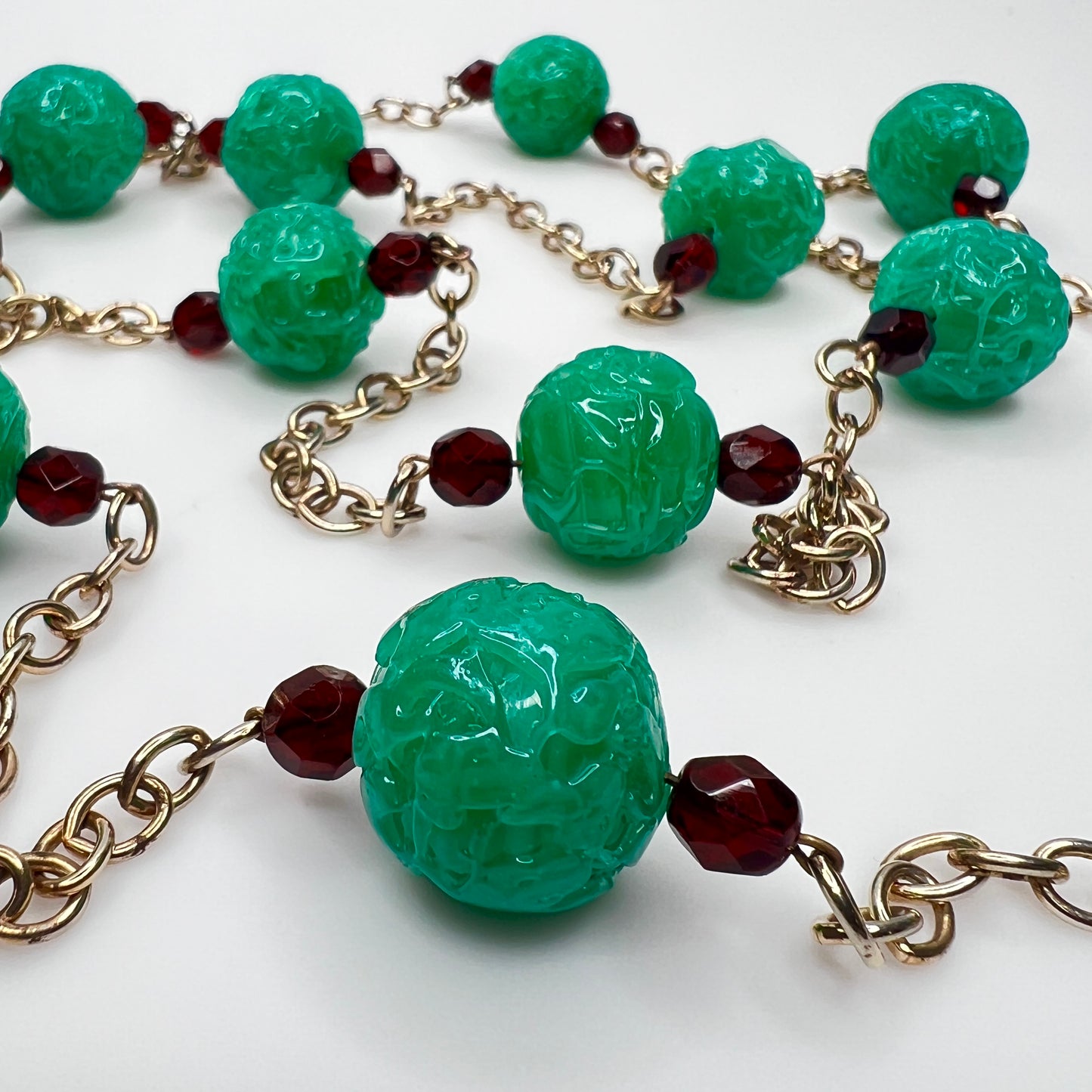 Close-up of textured green art glass beads with red faceted accents and gold chain