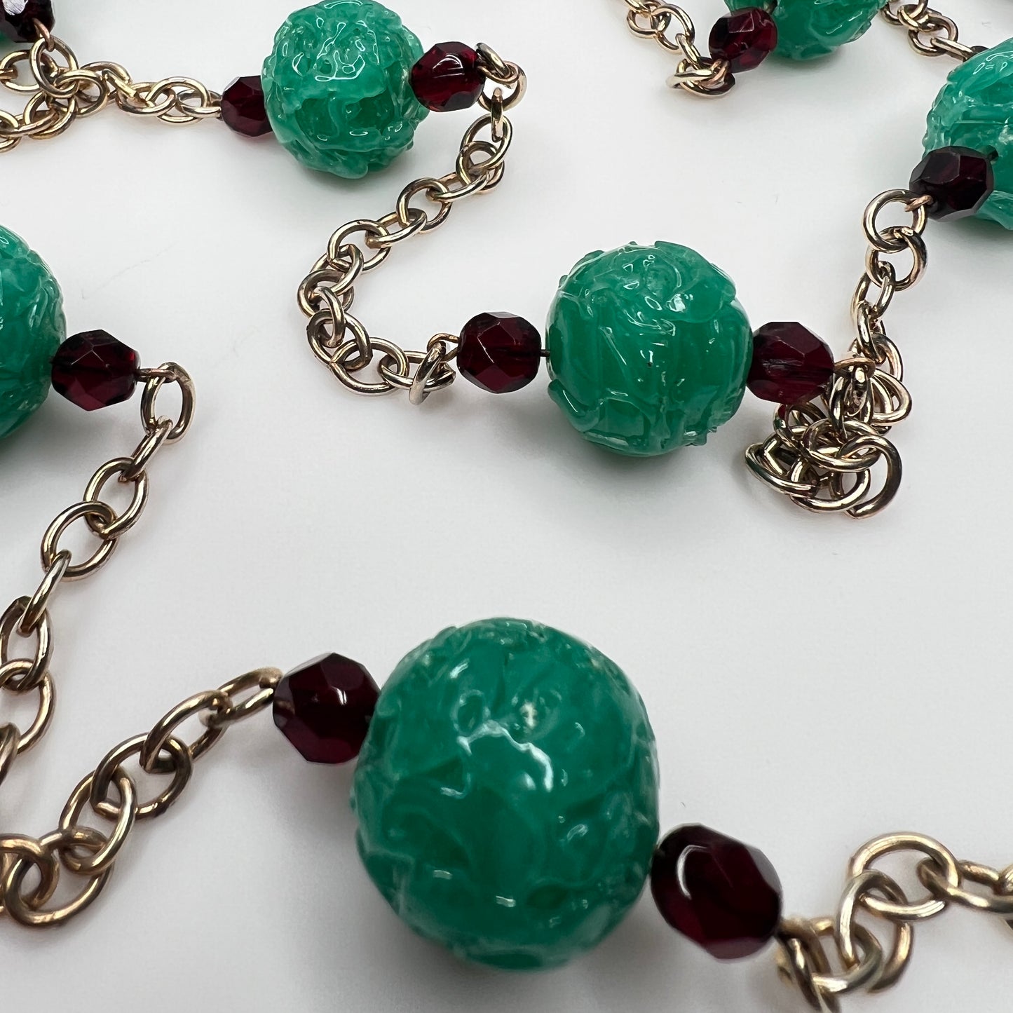 Close-up of textured green art glass beads with red faceted accents and gold chain