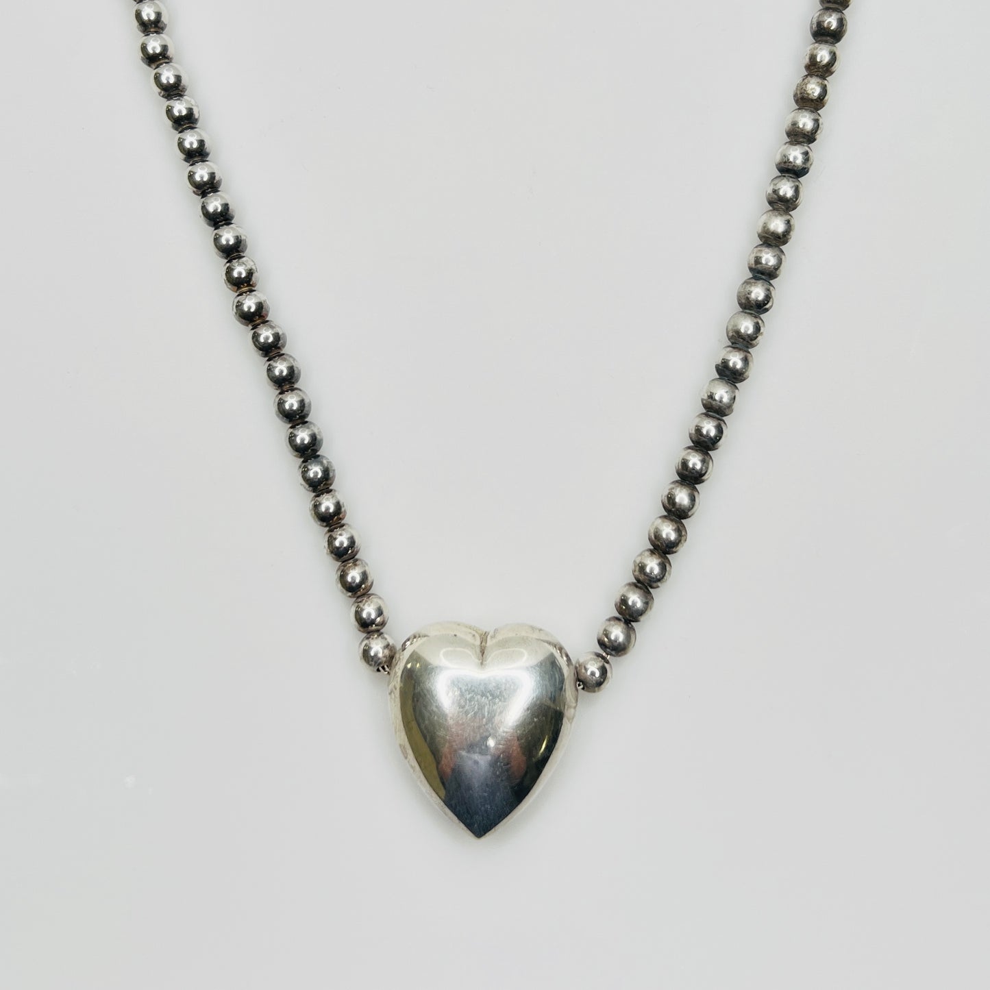 Close-up of silver puff heart pendant on white background
