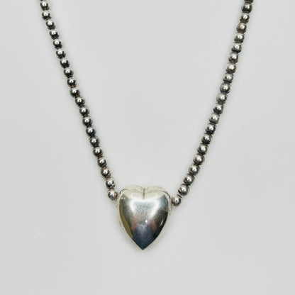 Close-up of silver puff heart pendant on white background