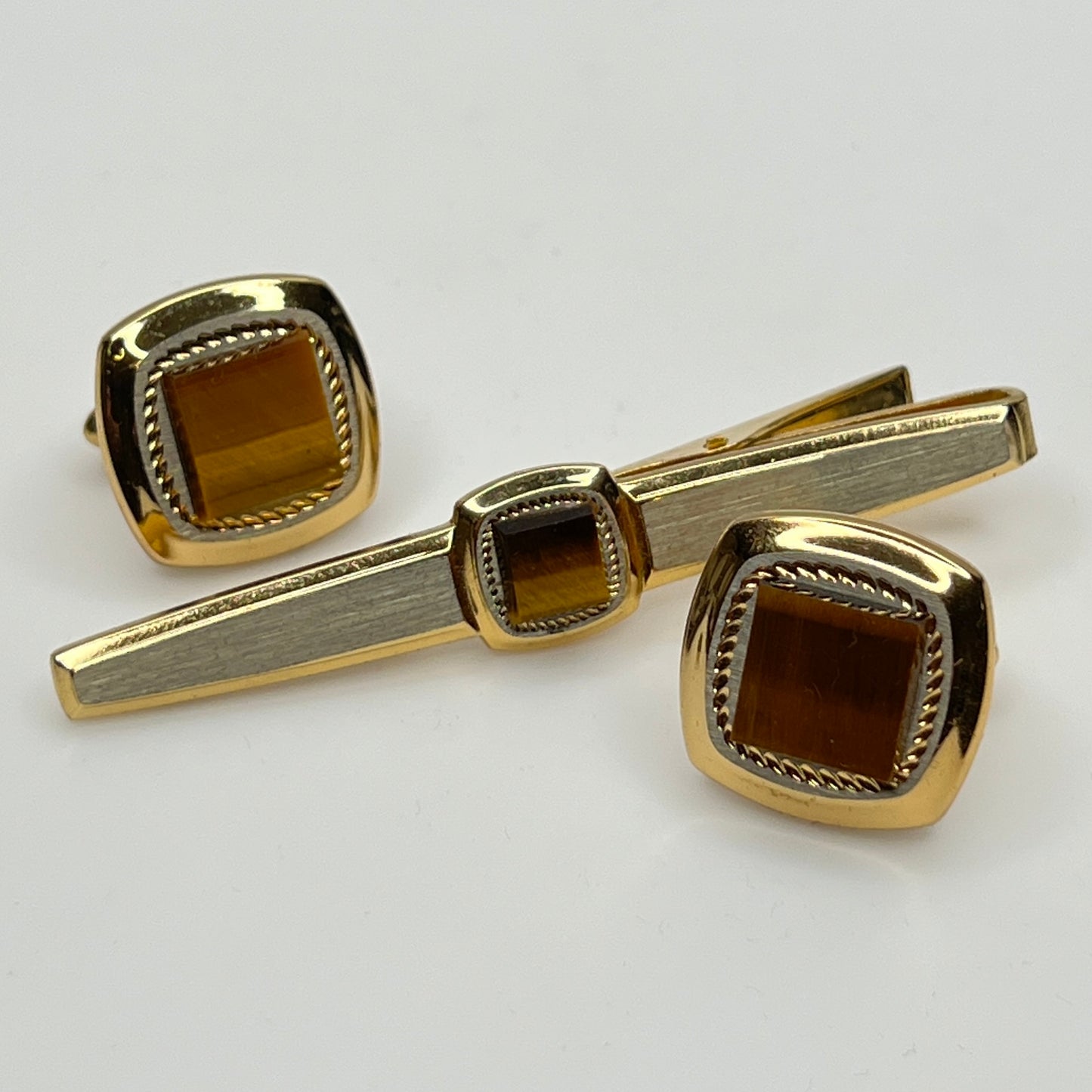 Gold tiger's eye cufflinks and tie clip set on a light gray background