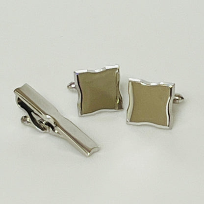 Silver tie clip and cufflinks on a light gray background