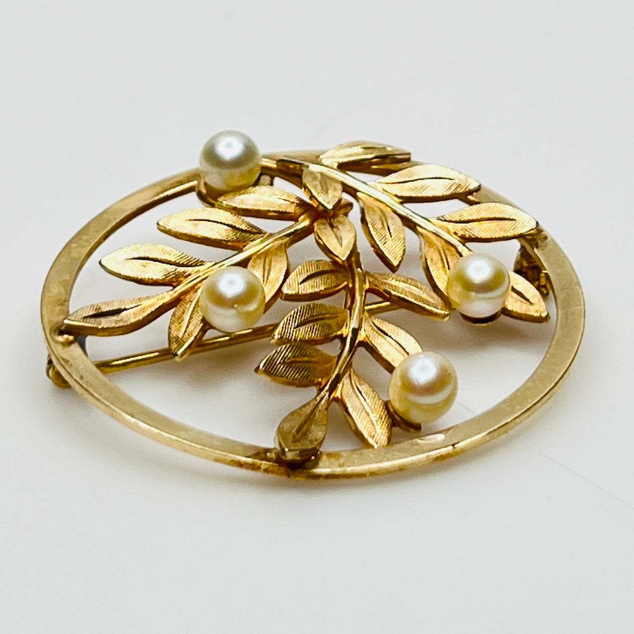 Close-up of brooch with textured gold leaves and five pearls