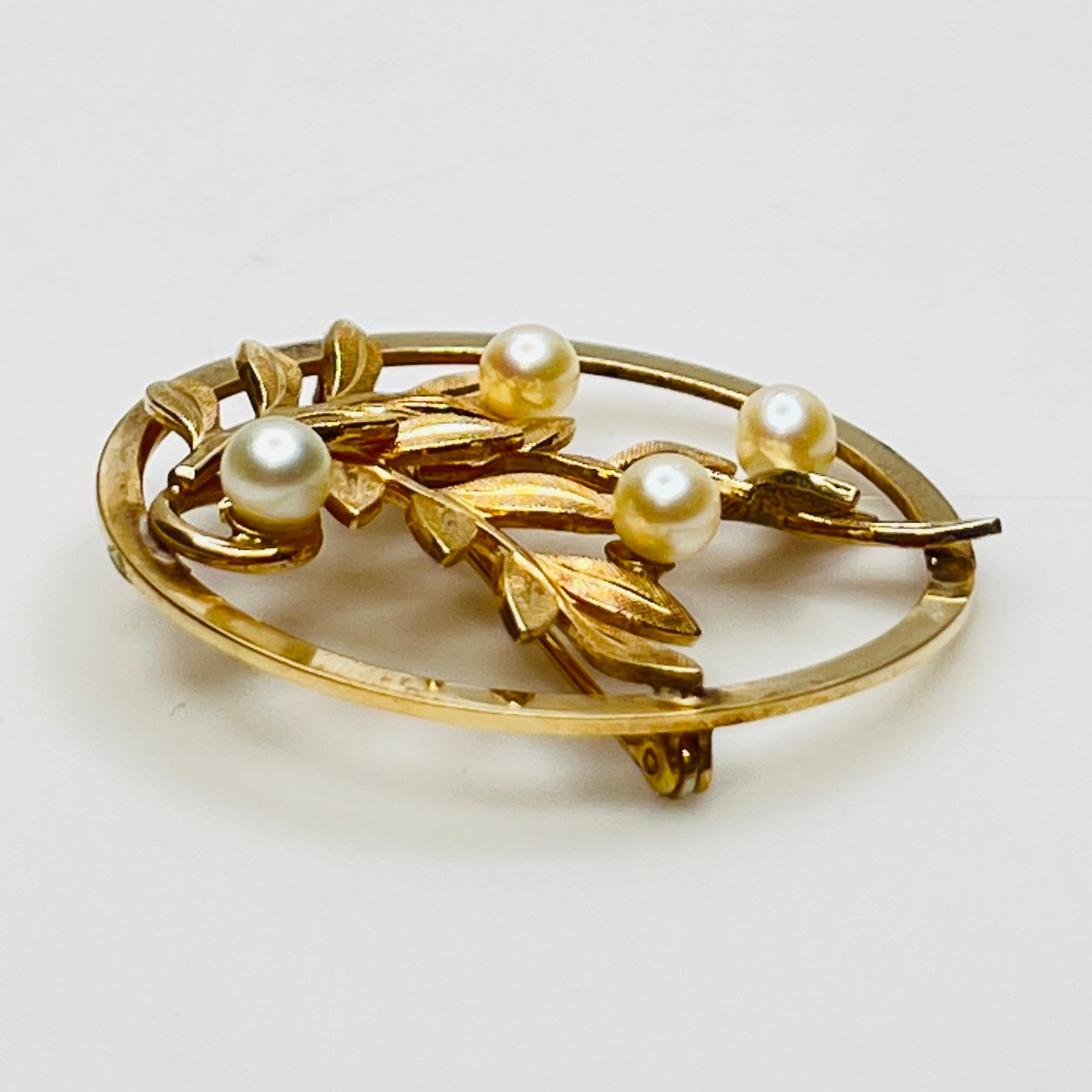 Close-up of brooch with textured gold leaves and five pearls