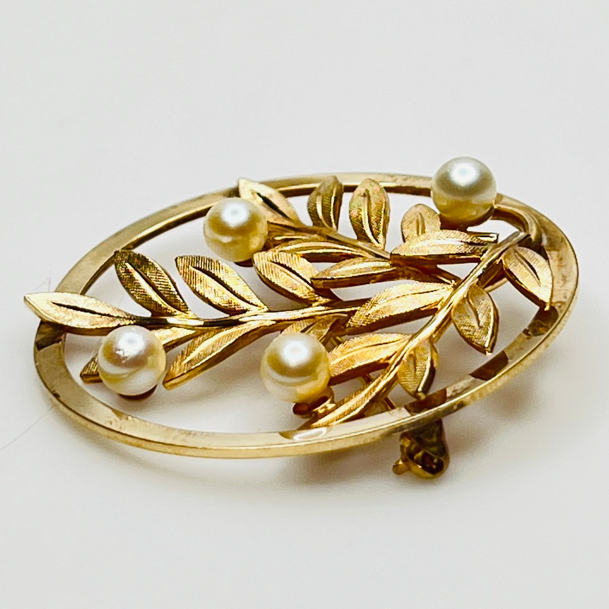 Close-up of brooch with textured gold leaves and five pearls
