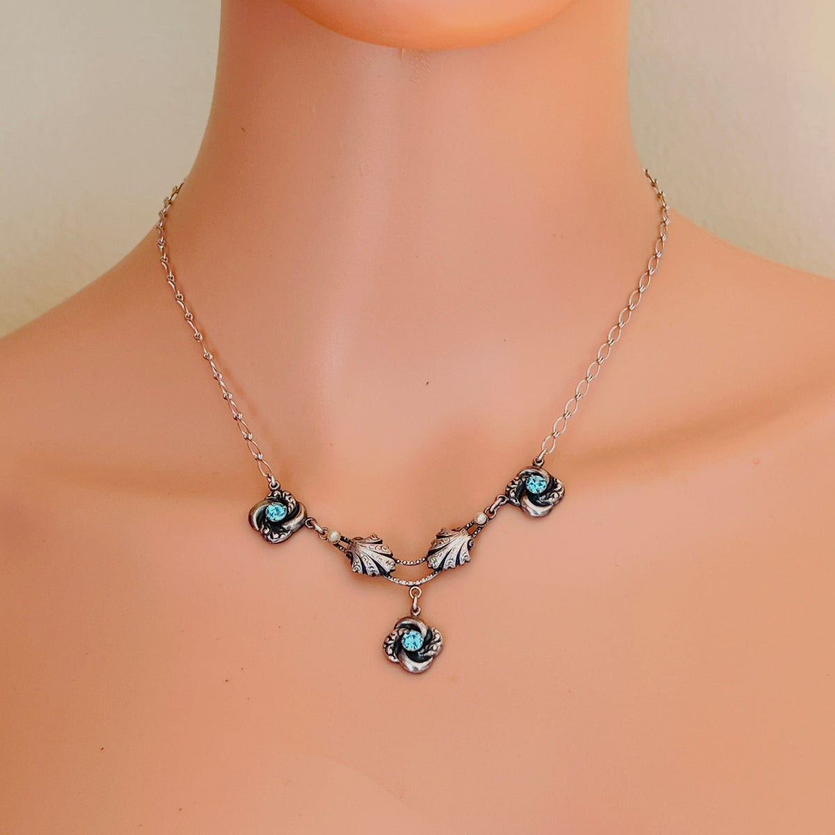 1960s silver-tone aqua rhinestone floral necklace displayed on mannequin showing delicate neckline placement.