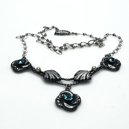Side view of vintage silver-tone necklace showing dimensional floral ornaments, textured chain and central pendant.