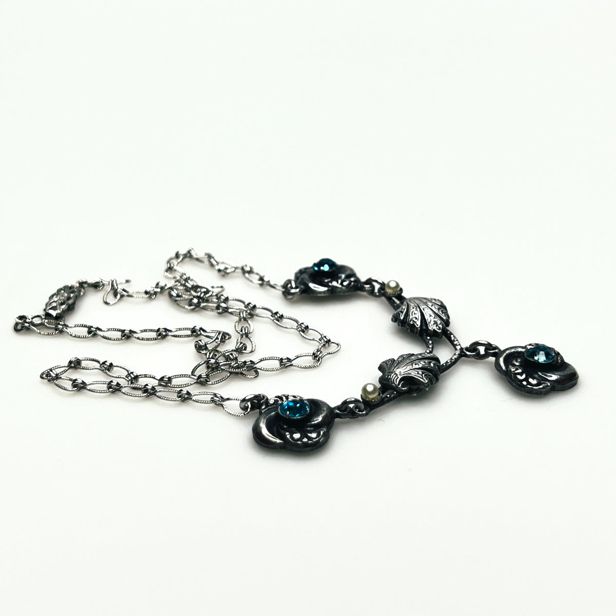 Side view of vintage silver-tone necklace showing dimensional floral ornaments, textured chain and central pendant.