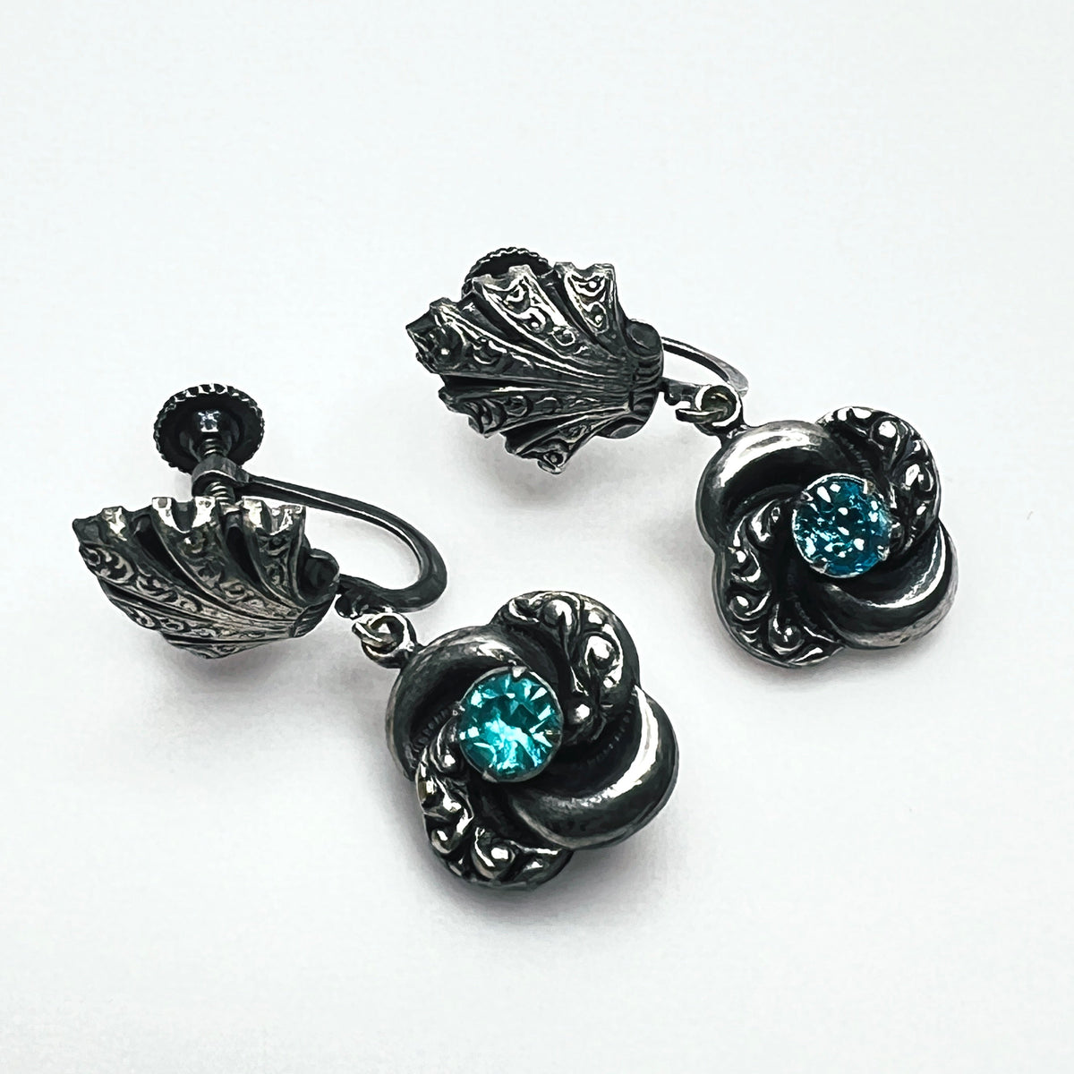 Close-up of vintage silver-tone screw-back earrings with aqua glass rhinestones and ornate floral dangles.