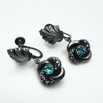 Close-up of vintage silver-tone screw-back earrings with aqua glass rhinestones and ornate floral dangles.