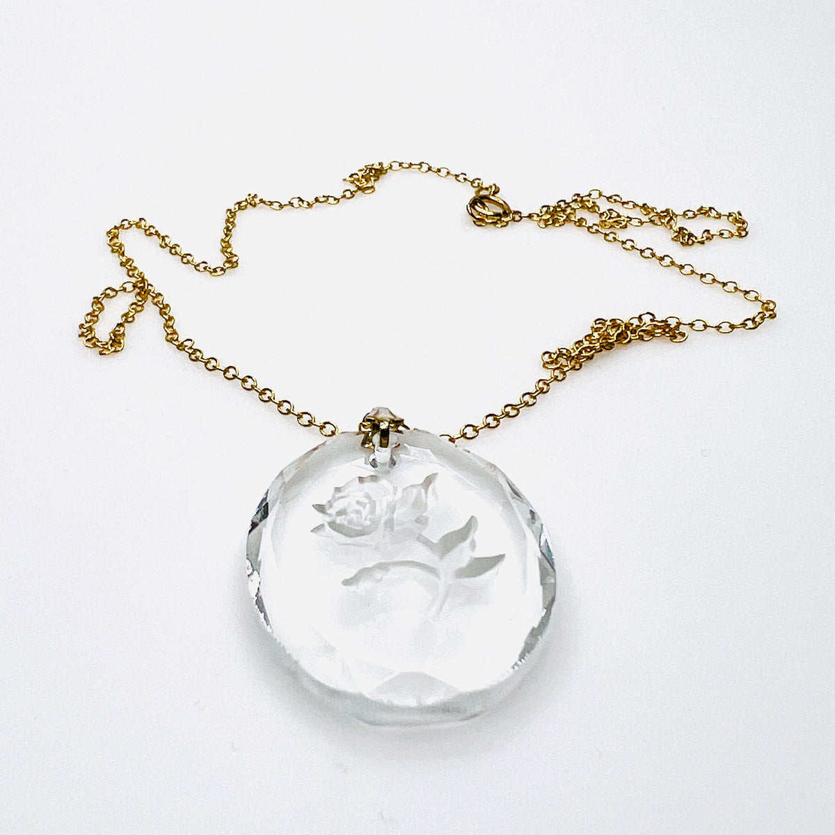 Side view of vintage oval crystal rose pendant showing its thickness, faceted edges, dimensional floral carving and gold tone bail.