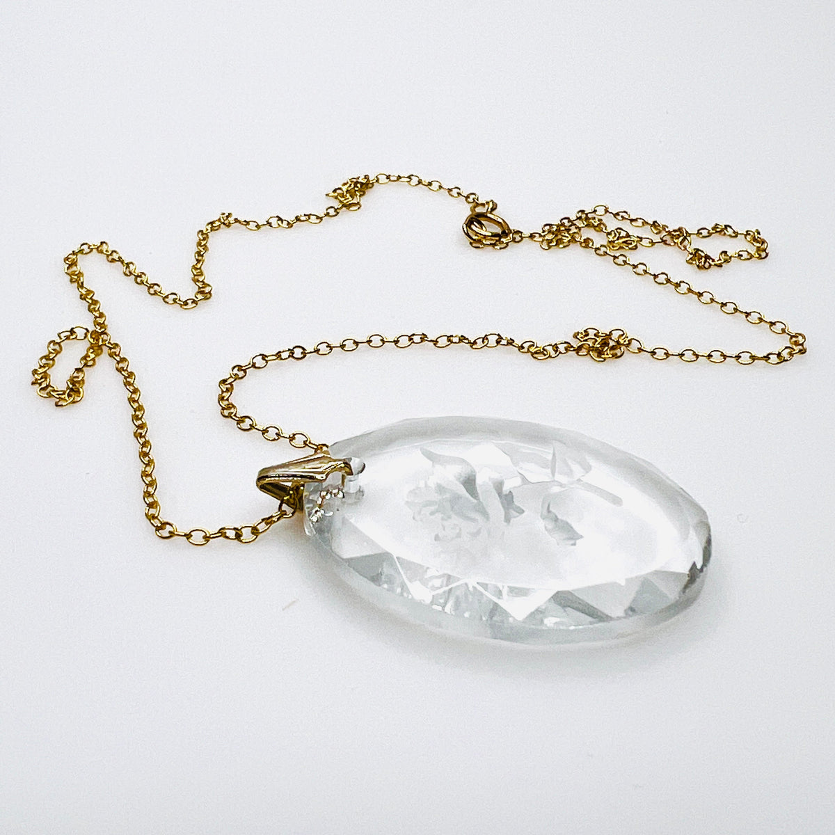 Side view of vintage oval crystal rose pendant showing its thickness, faceted edges, dimensional floral carving and gold tone bail.