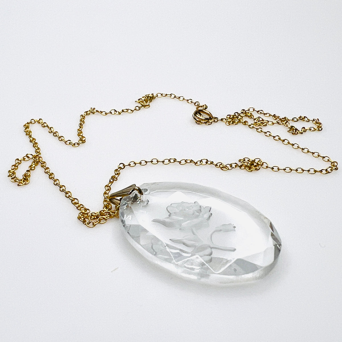 Side view of vintage oval crystal rose pendant showing its thickness, faceted edges, dimensional floral carving and gold tone bail.