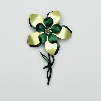 Vintage 1970s oversized green enamel flower brooch with layered emerald and chartreuse petals, green rhinestone center, and sculptural black stem.