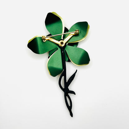 Reverse of vintage green enamel flower brooch showing layered metal petals, black stem, and gold-tone rollover safety clasp.