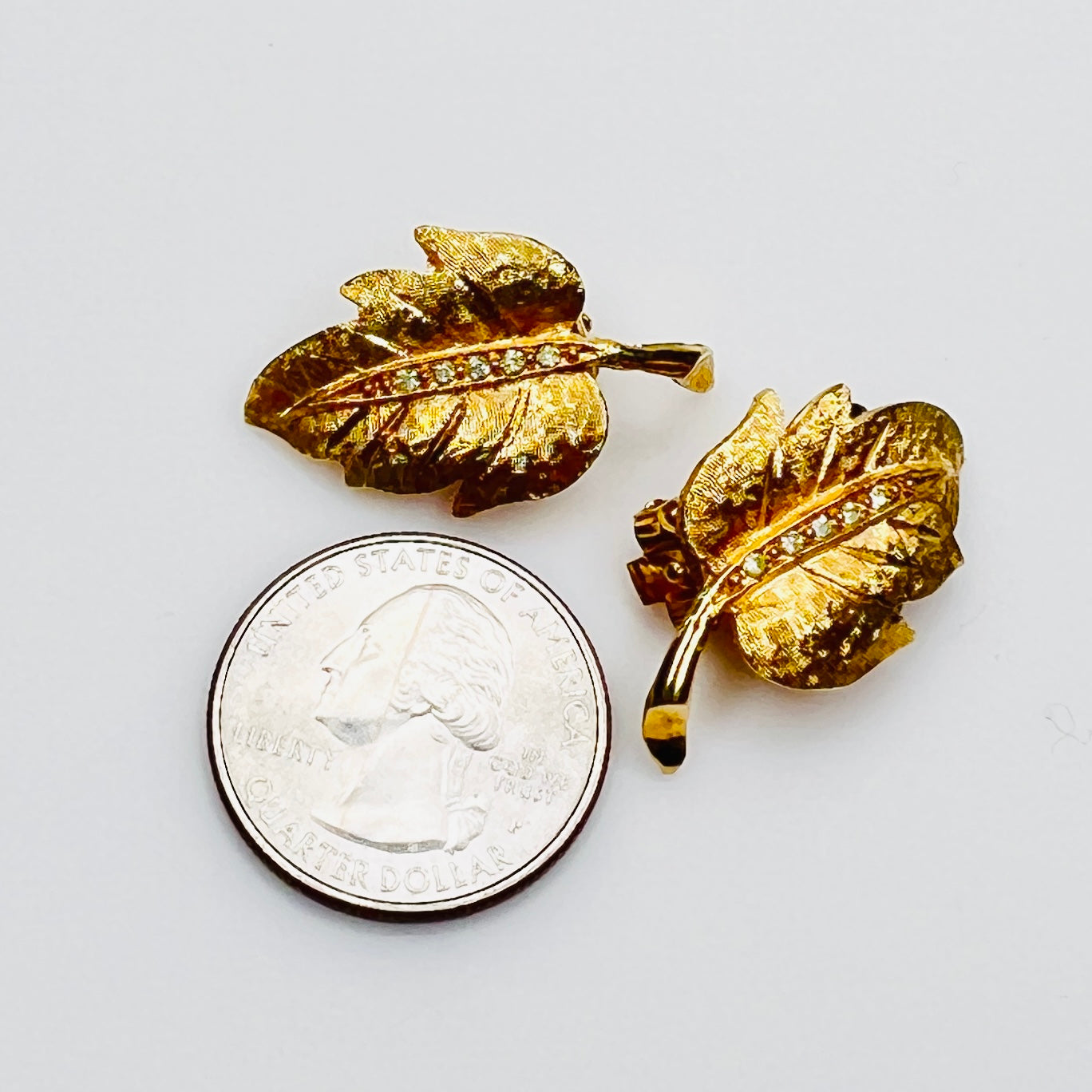 Signed Charel gold leaf earrings beside quarter