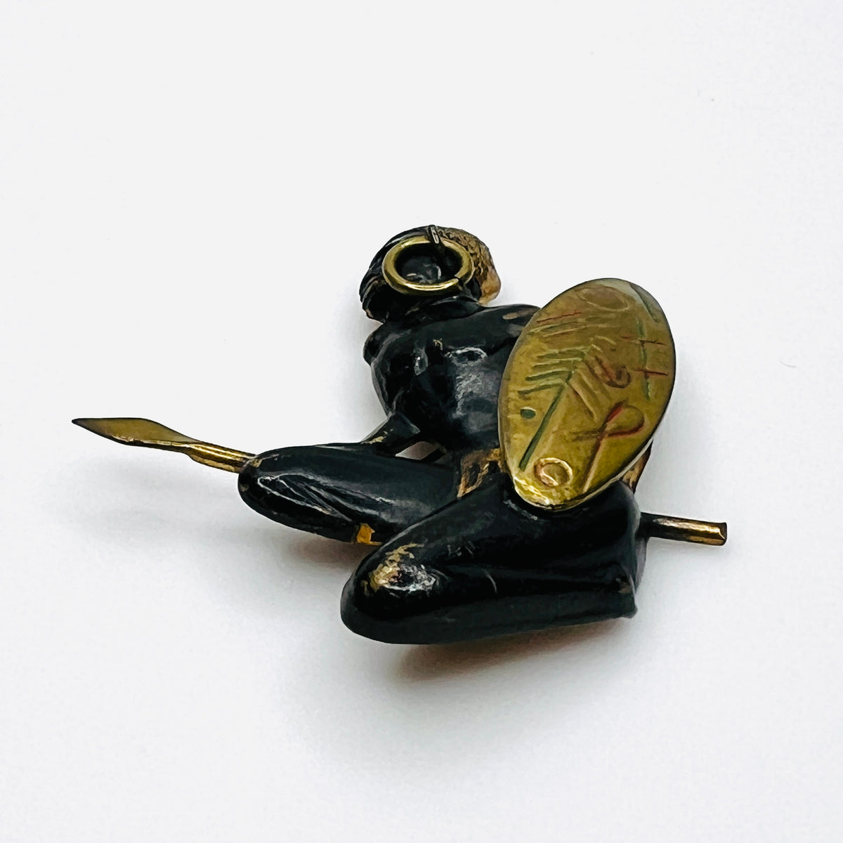 Angled view of mid-century African hunter brooch showing seated figure, brass-colored spear, and shield.