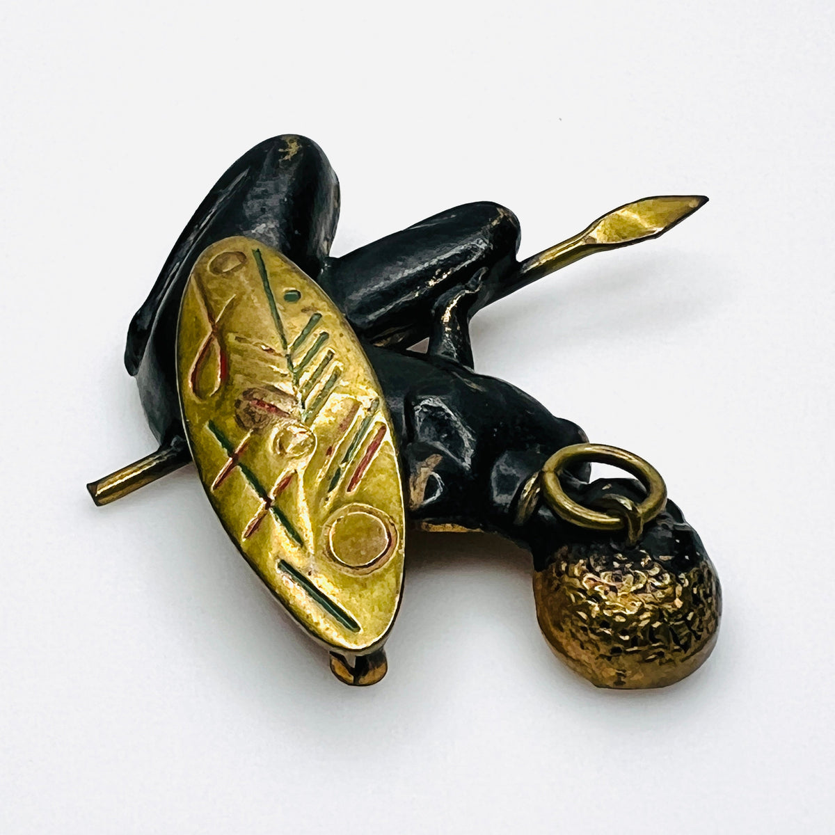 Side view of vintage African figural brooch highlighting dimensional metalwork and colorful shield details.