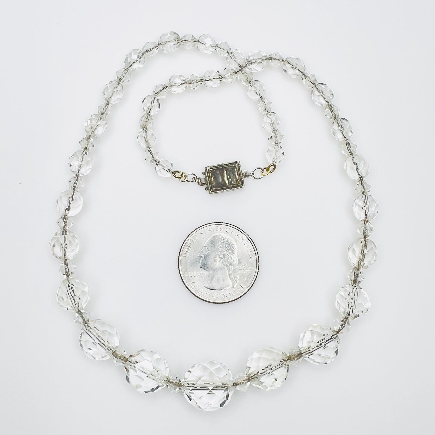 Vintage faceted crystal necklace beside quarter for scale