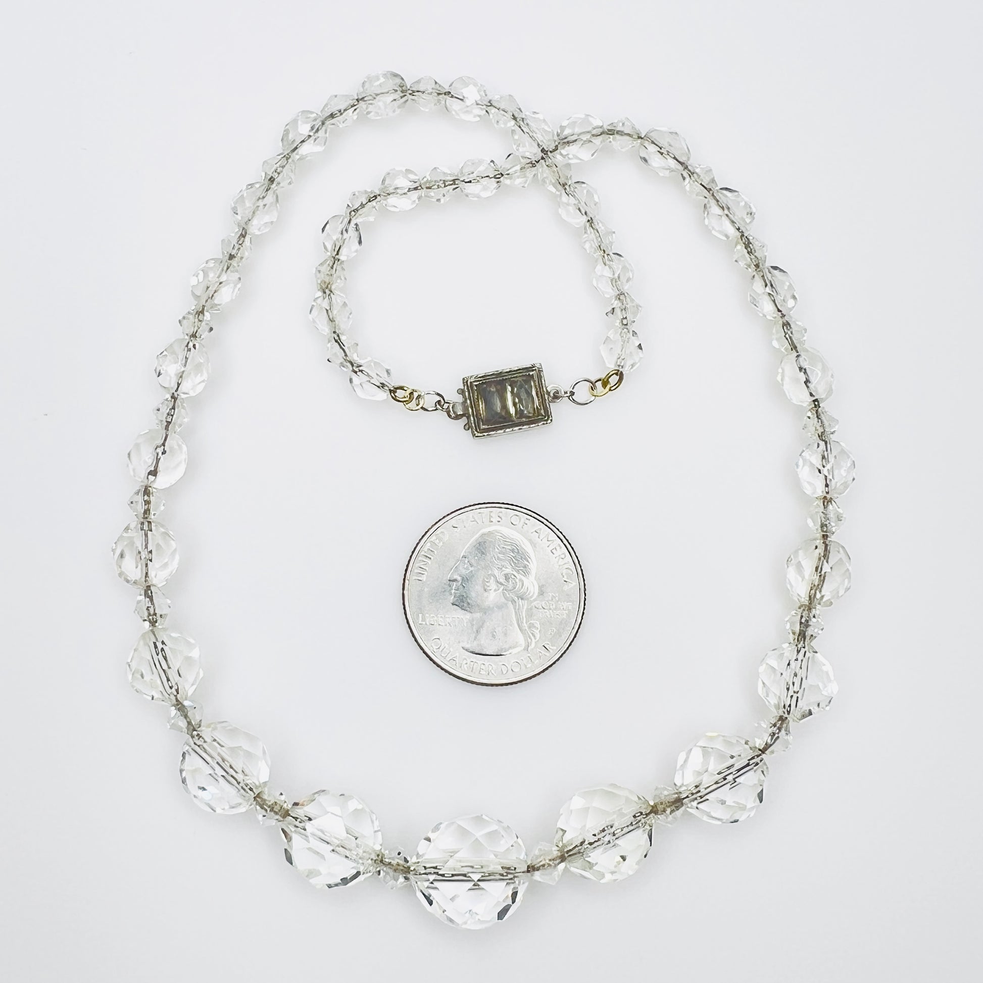 Vintage faceted crystal necklace beside quarter for scale