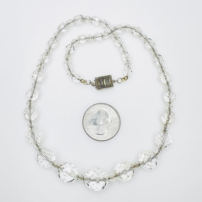 Vintage faceted crystal necklace beside quarter for scale