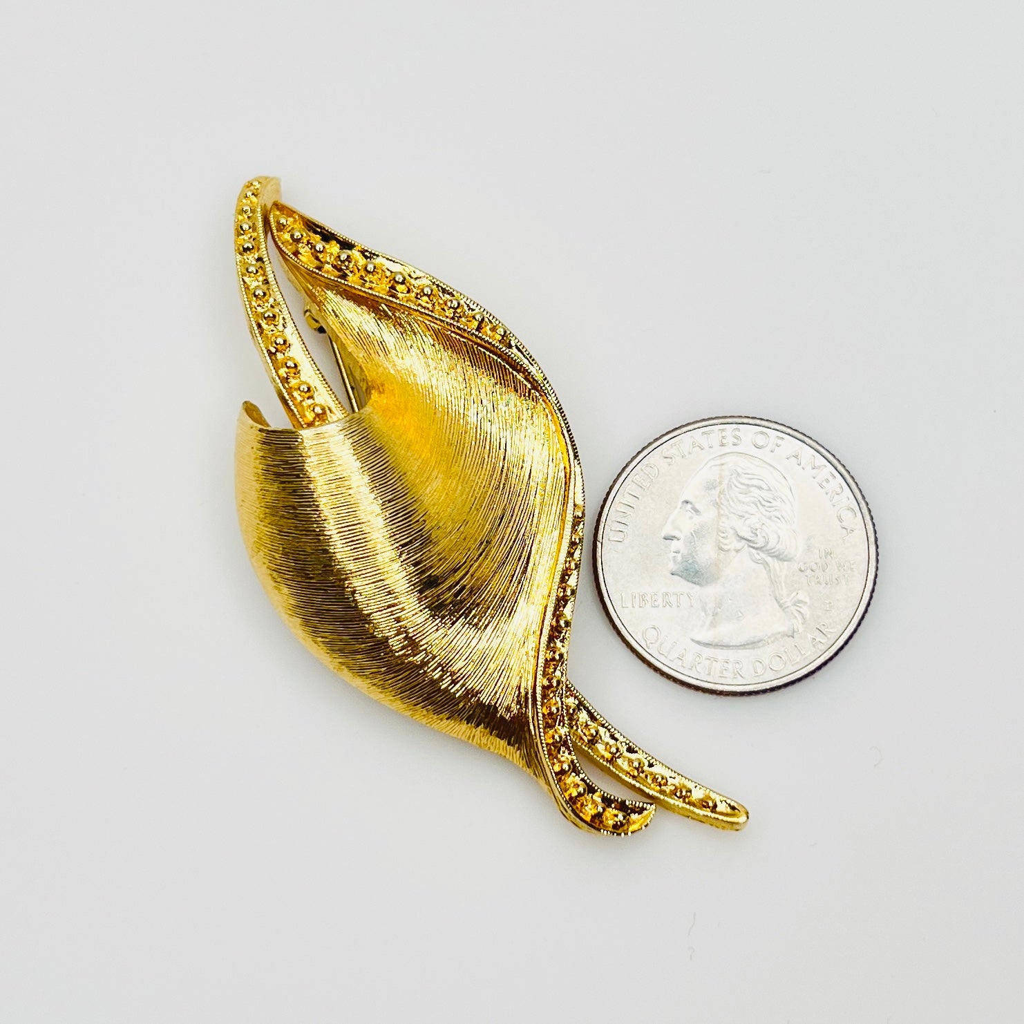 Signed Monet floral brooch beside quarter