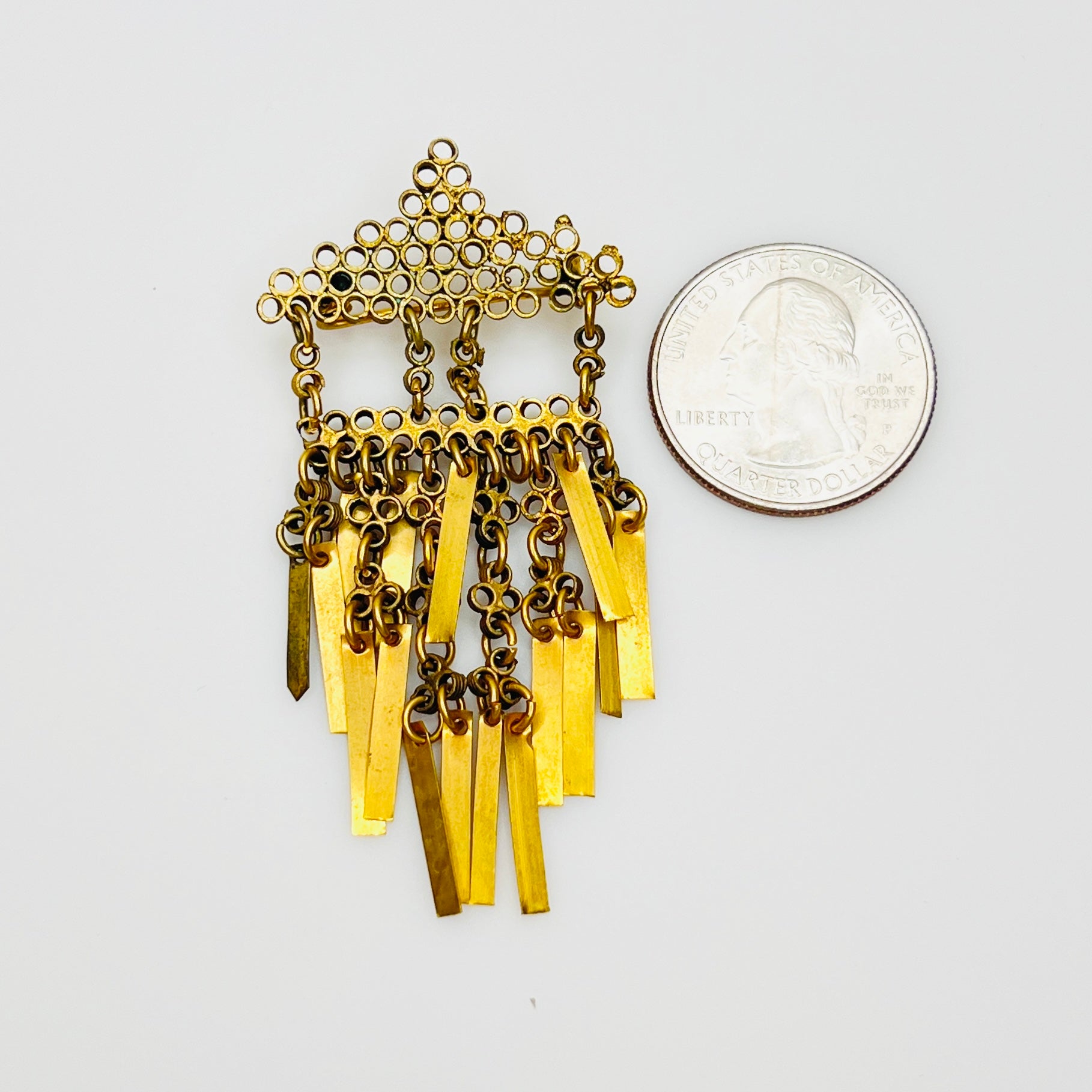 Vintage brass Art Deco tassel brooch beside quarter for scale