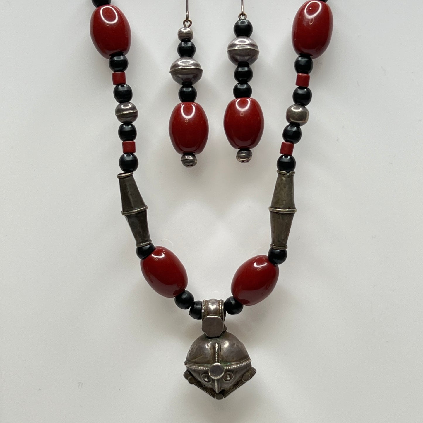 Beaded necklace and earrings with red, black, and silver beads on a white background