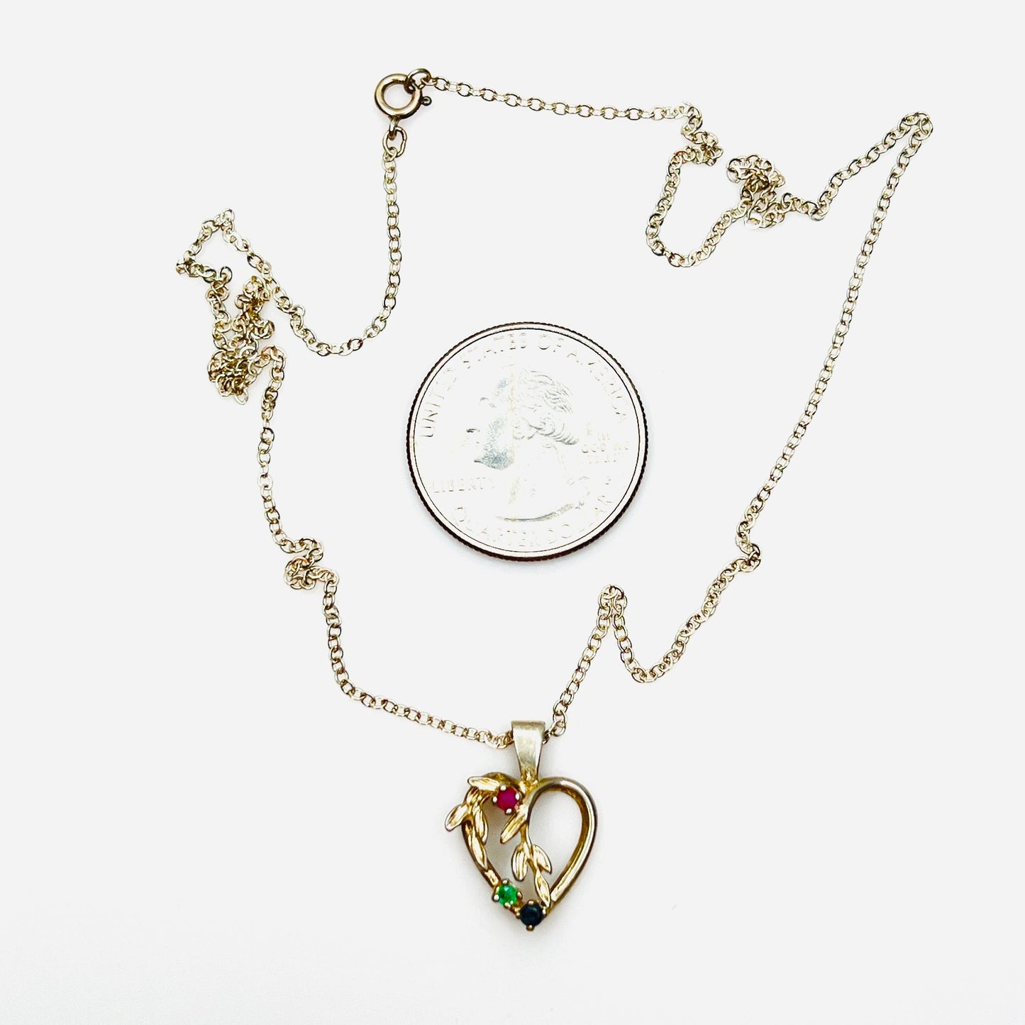 Vintage sterling silver heart pendant necklace beside quarter showing size and gemstone details.
