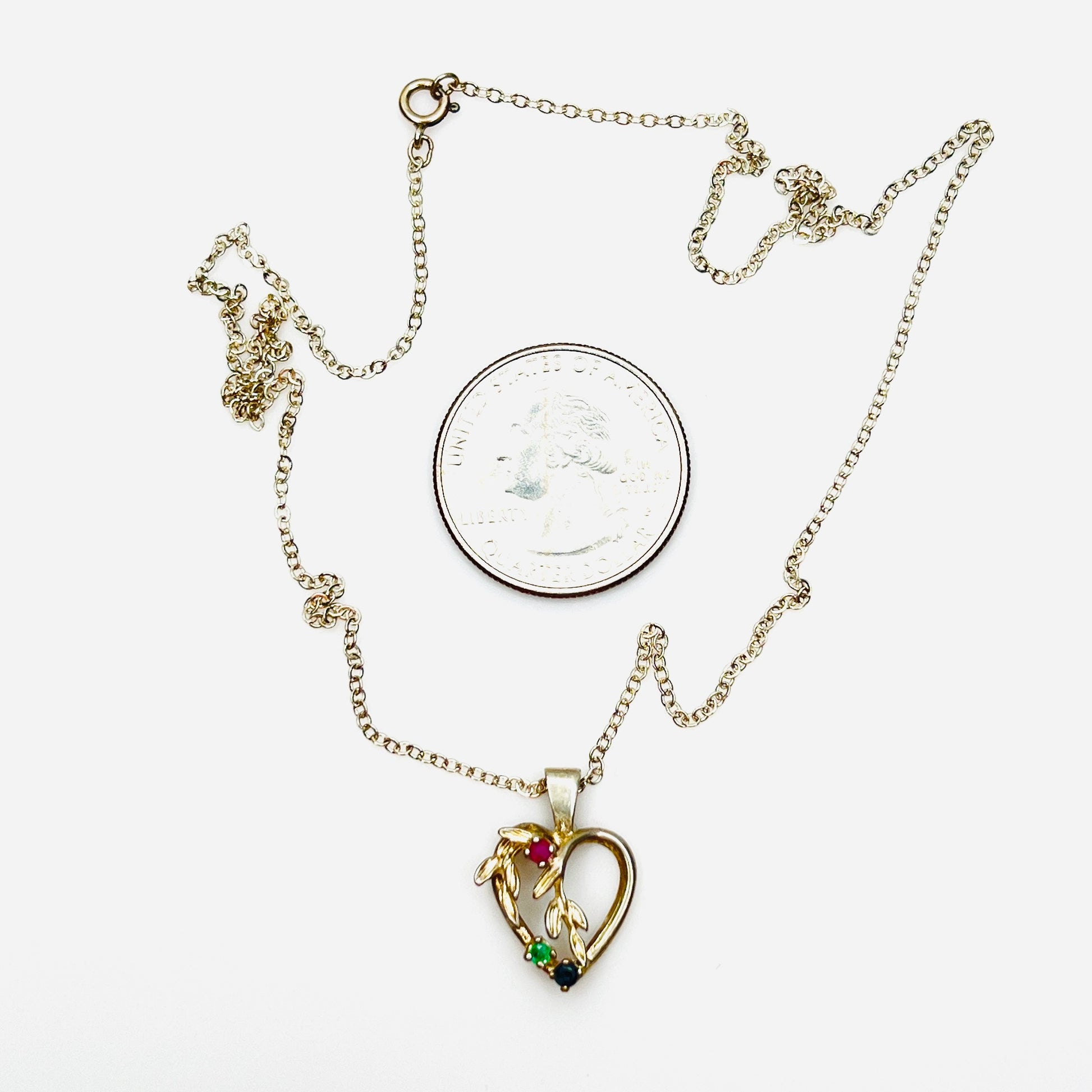 Vintage sterling silver heart pendant necklace beside quarter showing size and gemstone details.