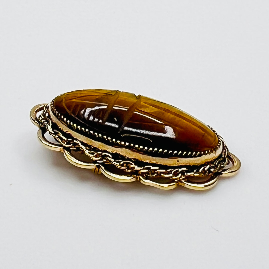 Side view of oval tiger’s eye brooch with high dome and scalloped gold setting