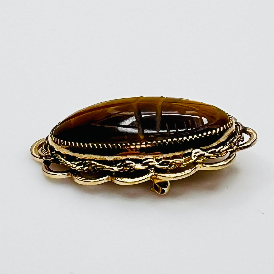 Side view of oval tiger’s eye brooch with high dome and scalloped gold setting