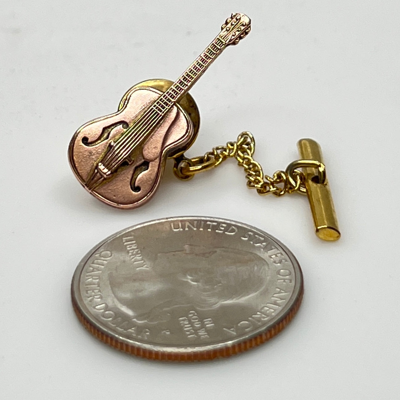 Vintage guitar tie tack next to quarter for size reference