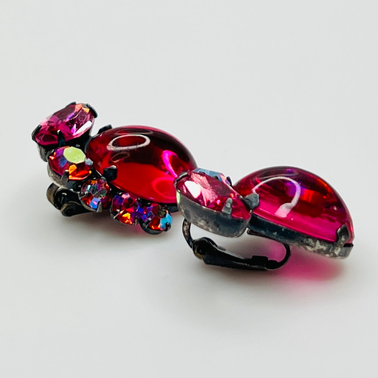 Pair of ornate earrings with pink and multicolored gemstones on a light gray background
