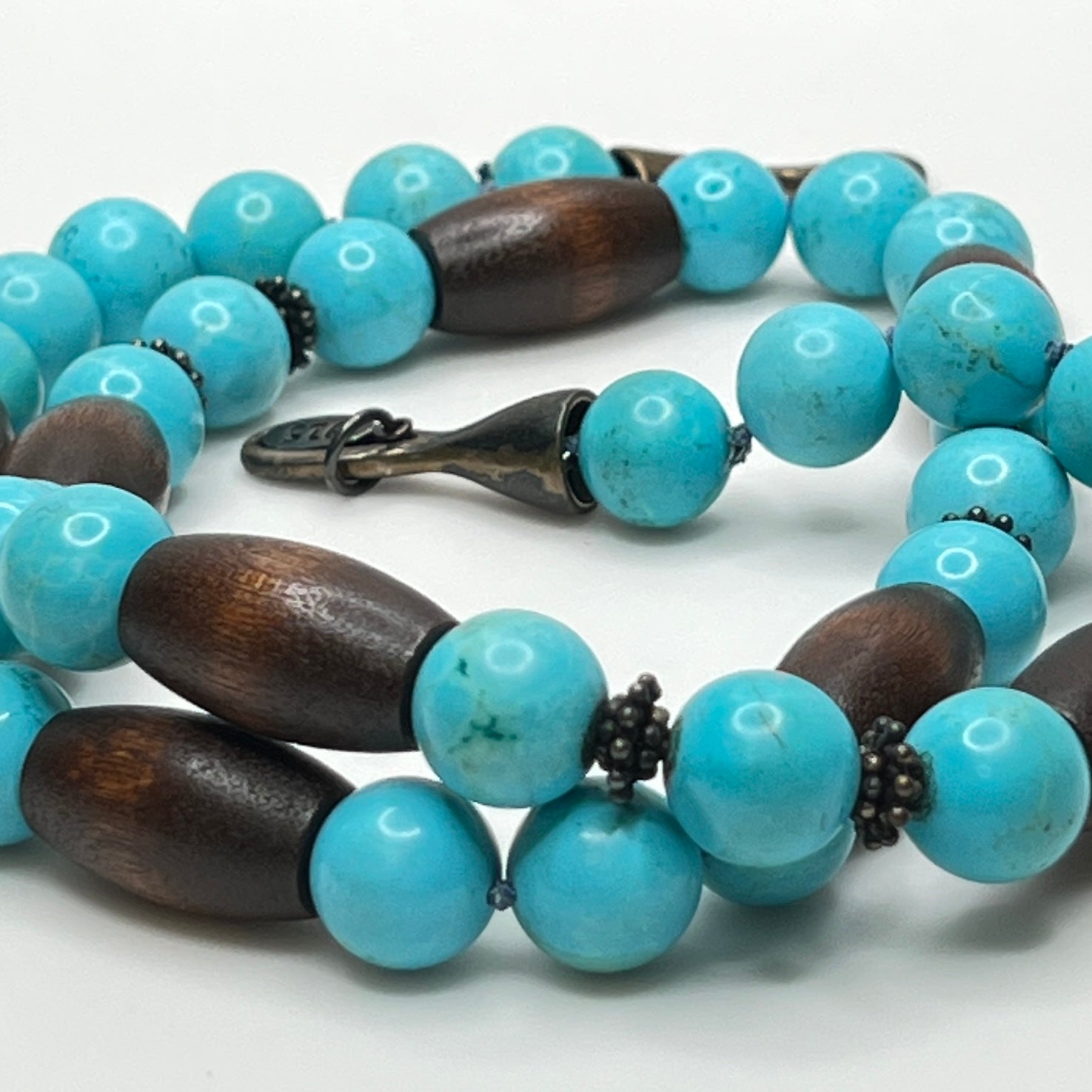 Close-up of EXEX tag and sterling hook clasp with turquoise and wood bead detail