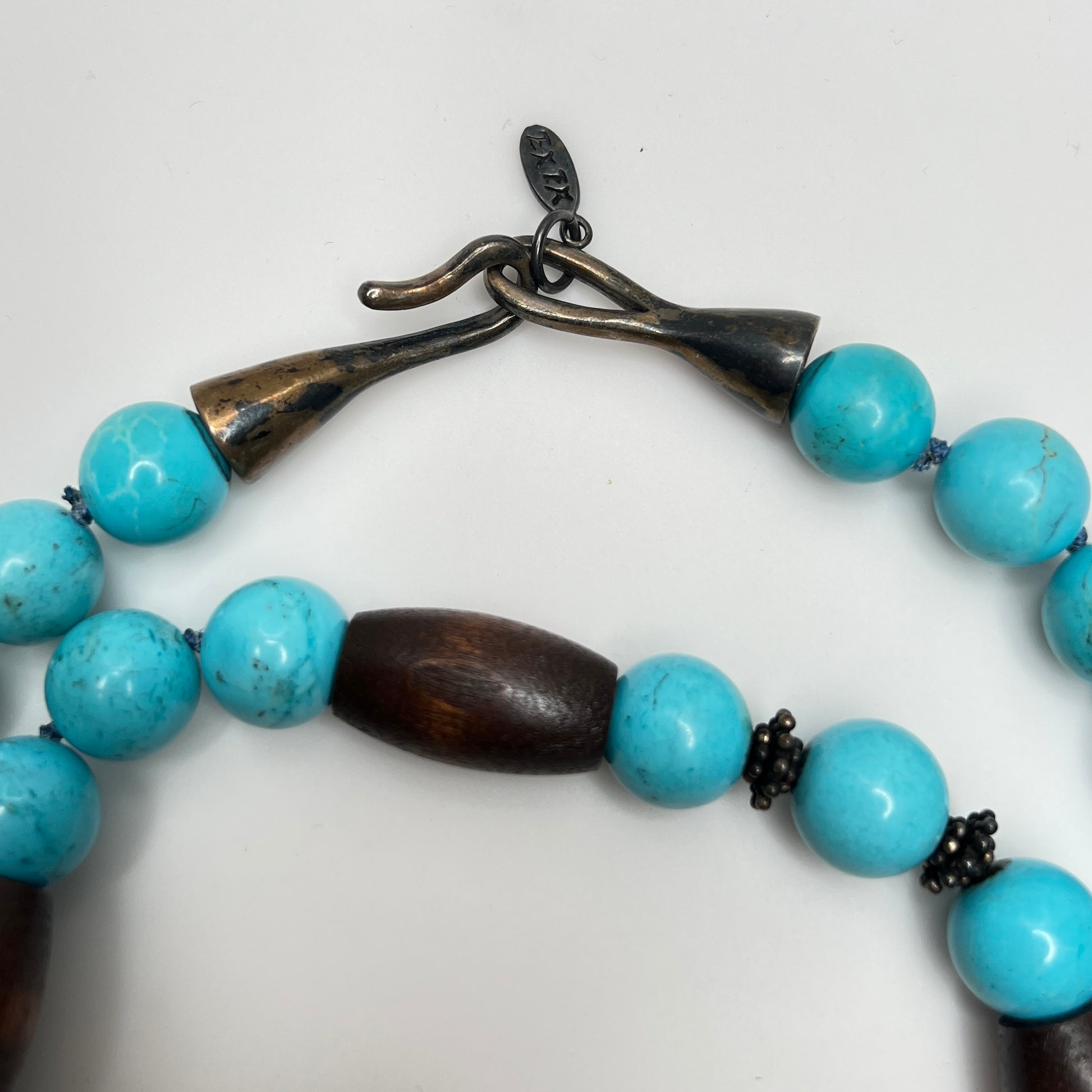 Close-up of EXEX tag and sterling hook clasp with turquoise and wood bead detail