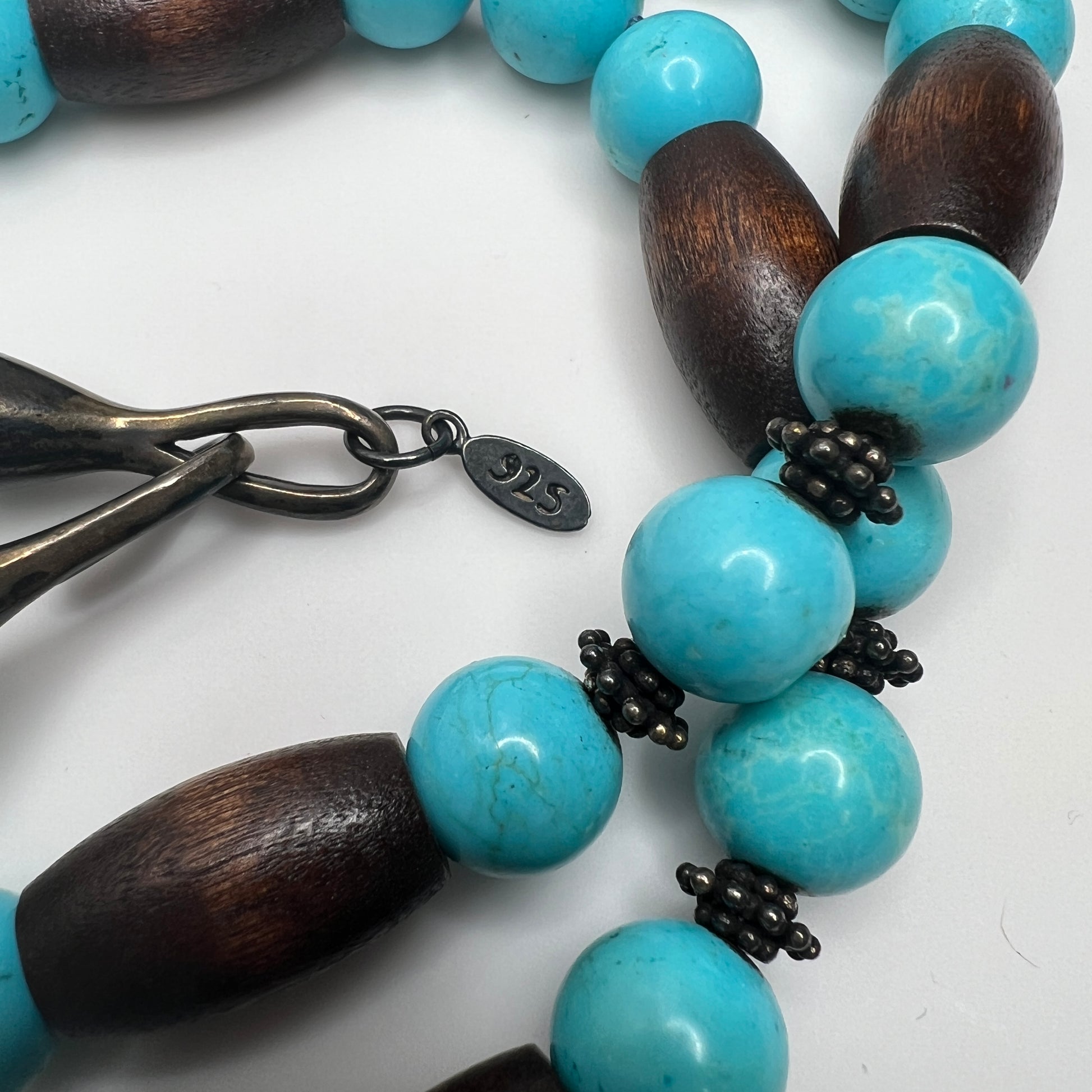 Close-up of EXEX tag and sterling hook clasp with turquoise and wood bead detail