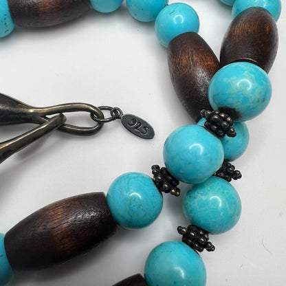 Close-up of EXEX tag and sterling hook clasp with turquoise and wood bead detail