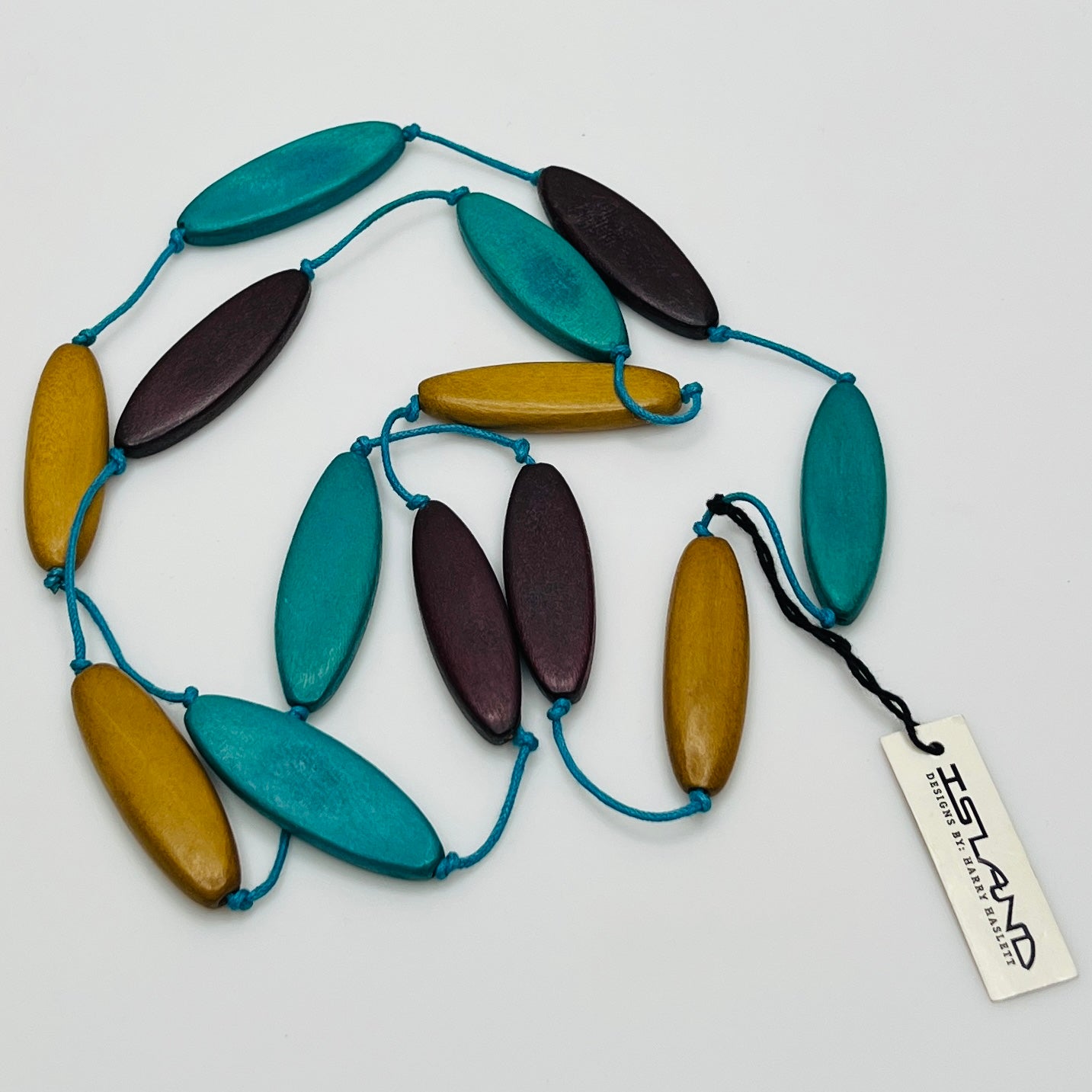 Harry Haslett Island Design necklace with long oval wood beads in teal, plum, and mustard on turquoise cord.