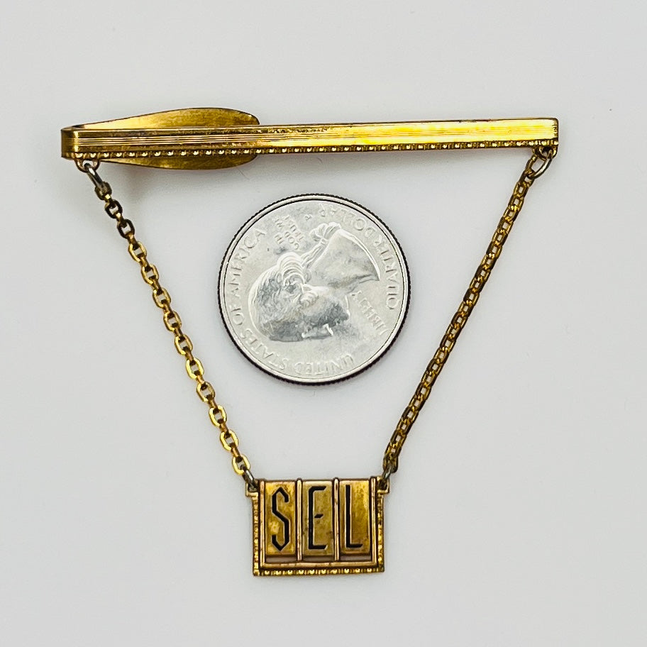 Full view of midcentury monogram tie clip in gold-tone brass with quarter for scale