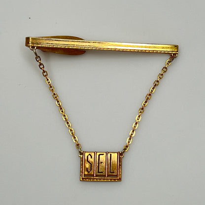 Full view of midcentury monogram tie clip in gold-tone brass