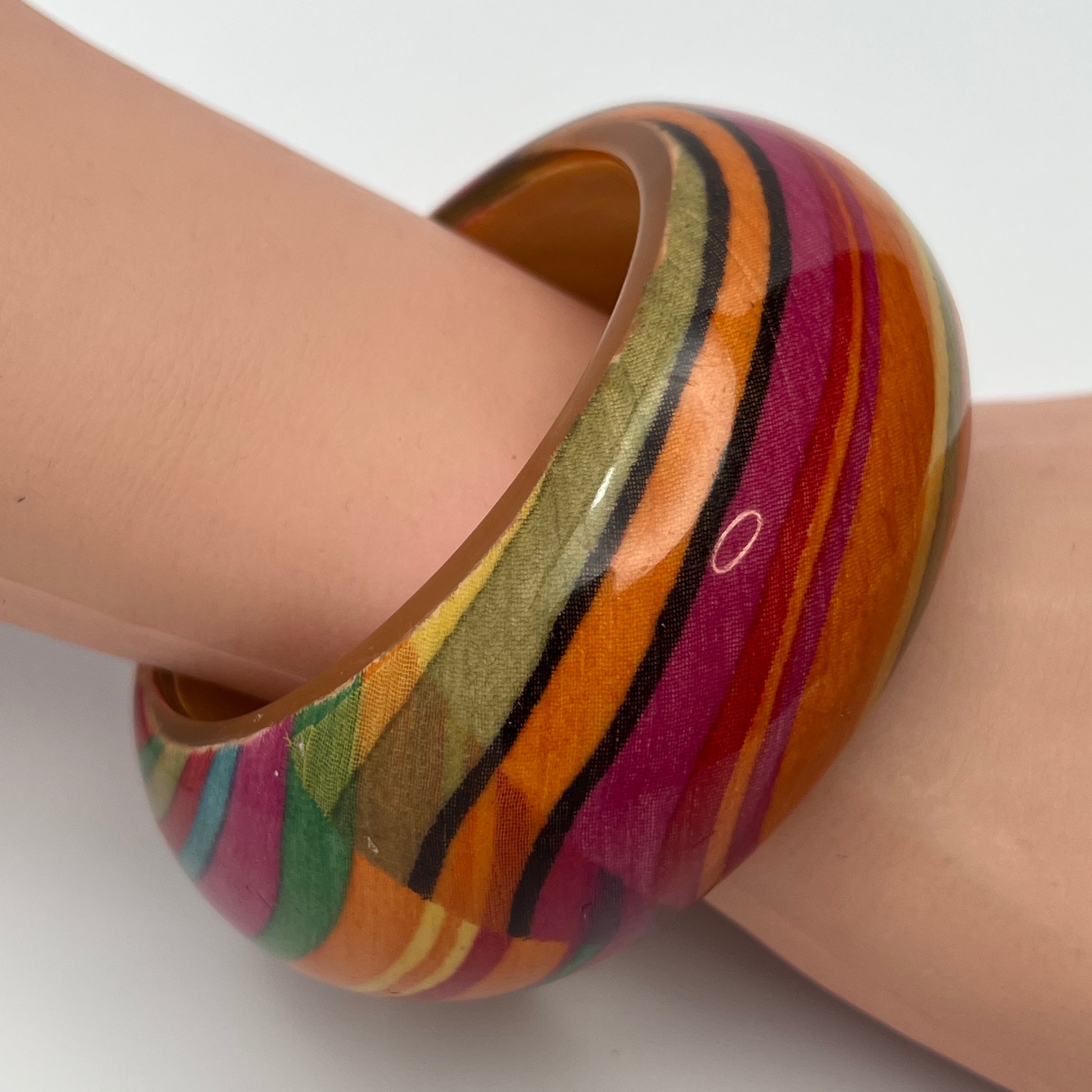 1970s domed lucite bangle with warm striped pattern on model's wrist
