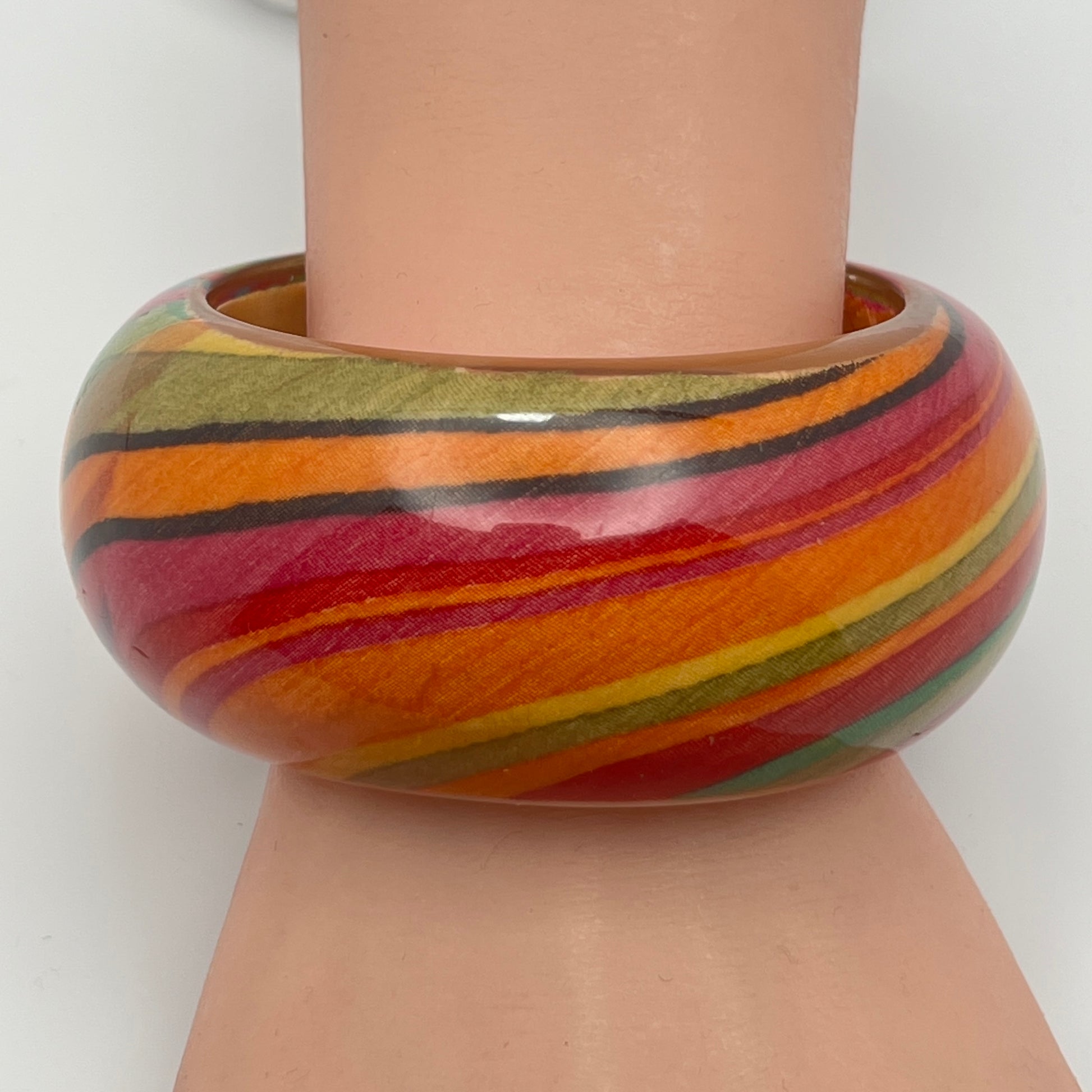 1970s domed lucite bangle with warm striped pattern on model's wrist