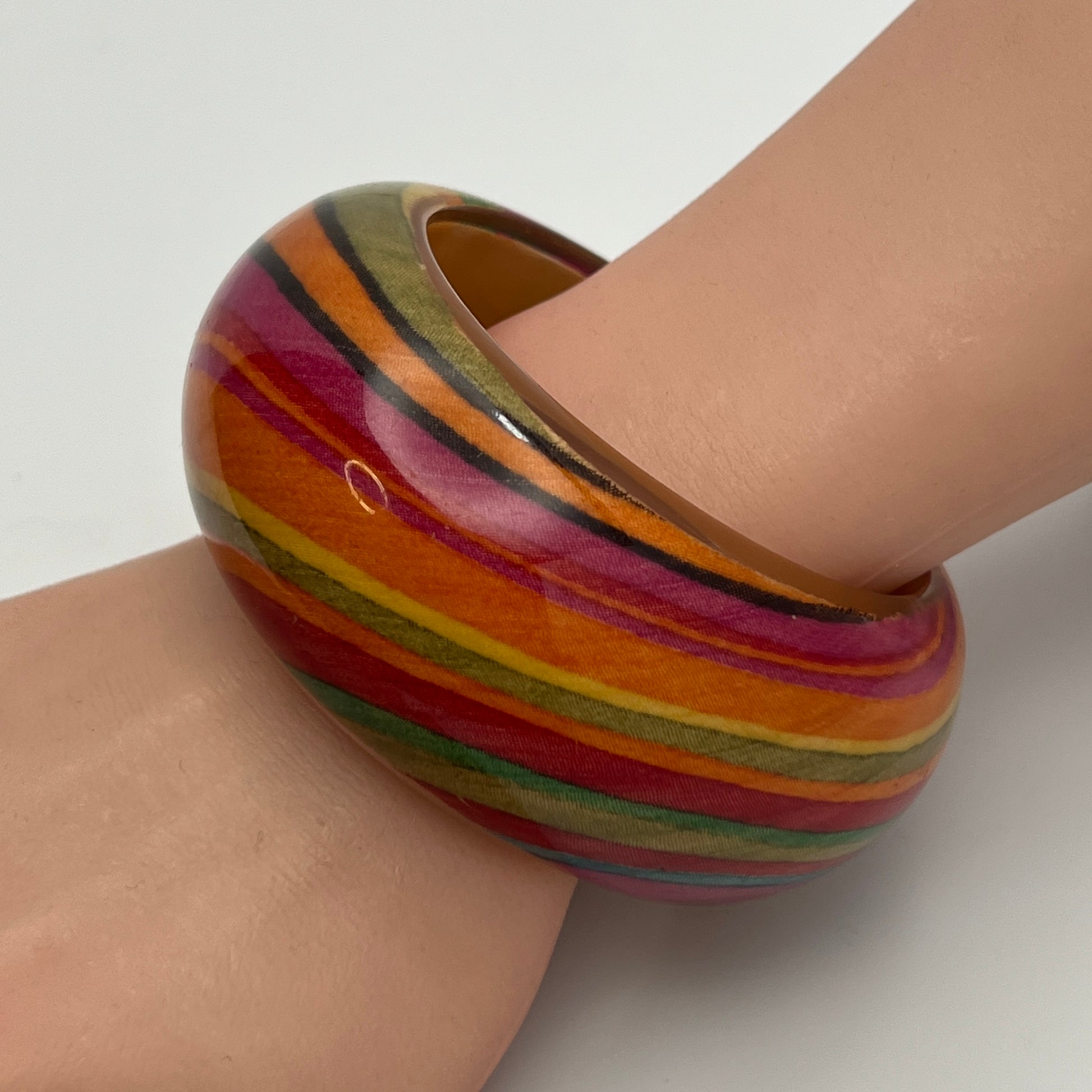 1970s domed lucite bangle with warm striped pattern on model's wrist