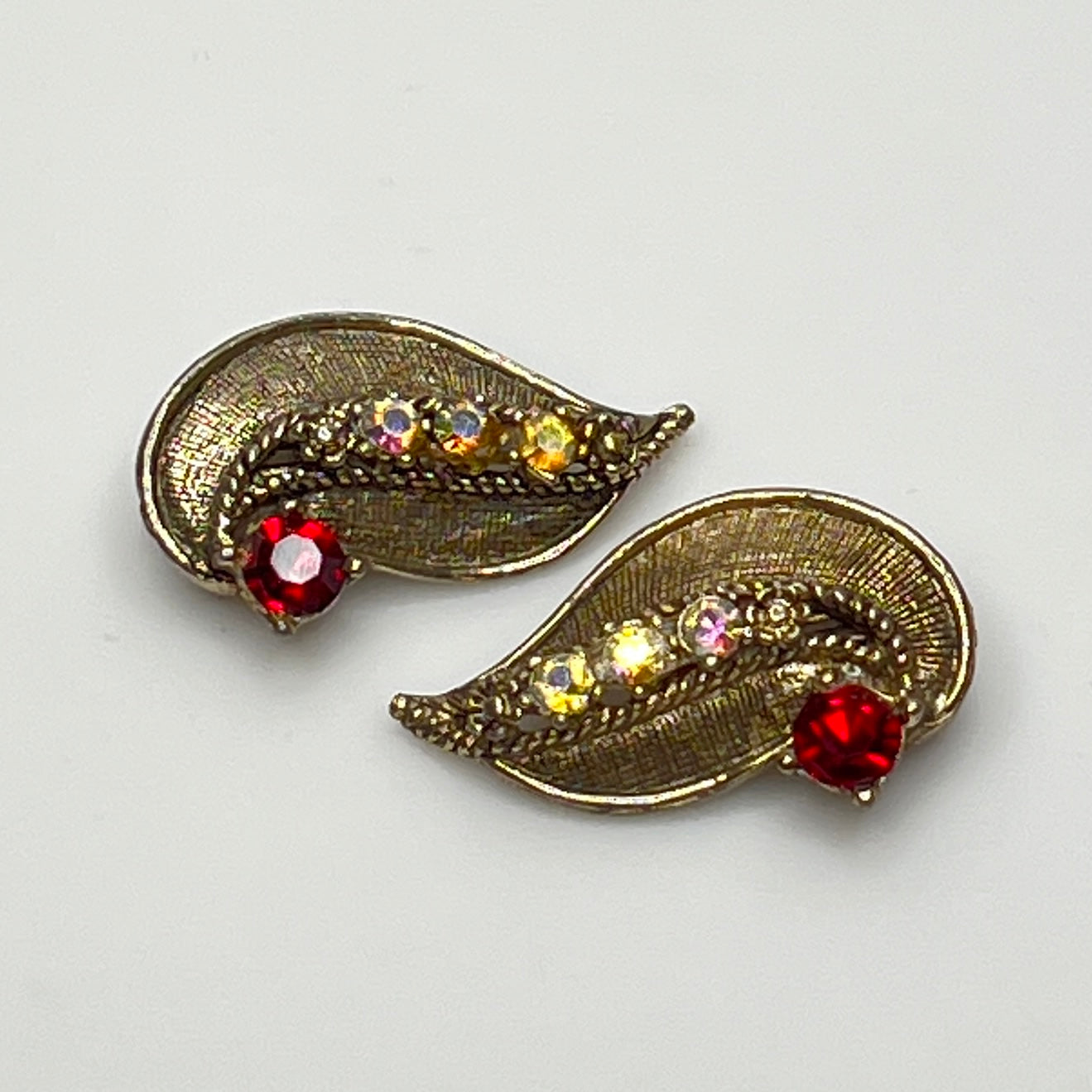 Pair of gold leaf-shaped earrings with gemstones on a light gray background