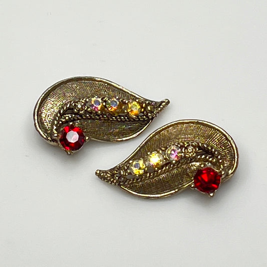 Pair of gold leaf-shaped earrings with gemstones on a light gray background