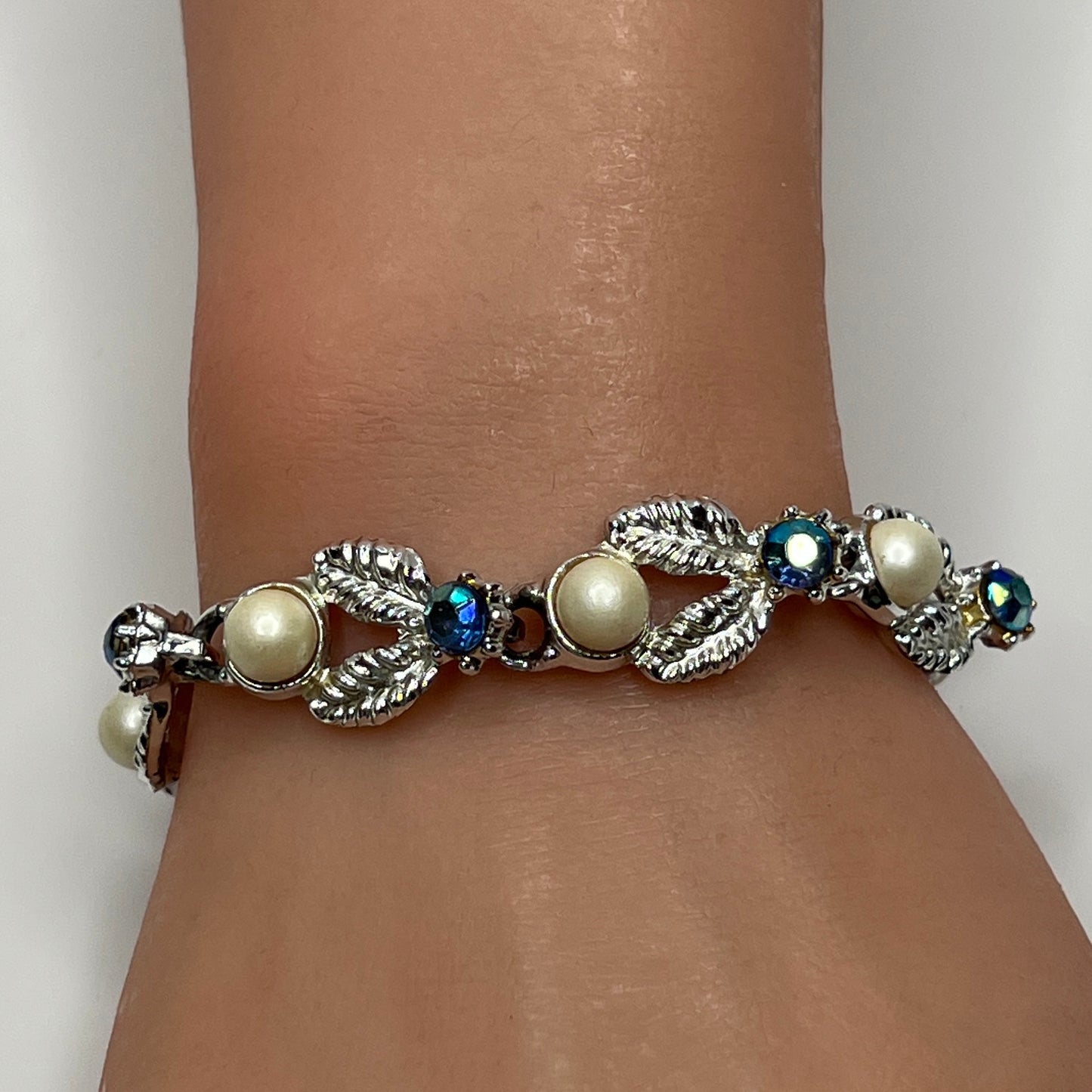 Silver leaf link bracelet with faux pearls and blue rhinestones worn on wrist