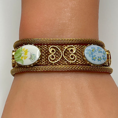 Gold mesh bracelet with hand-painted floral cabochons worn on wrist