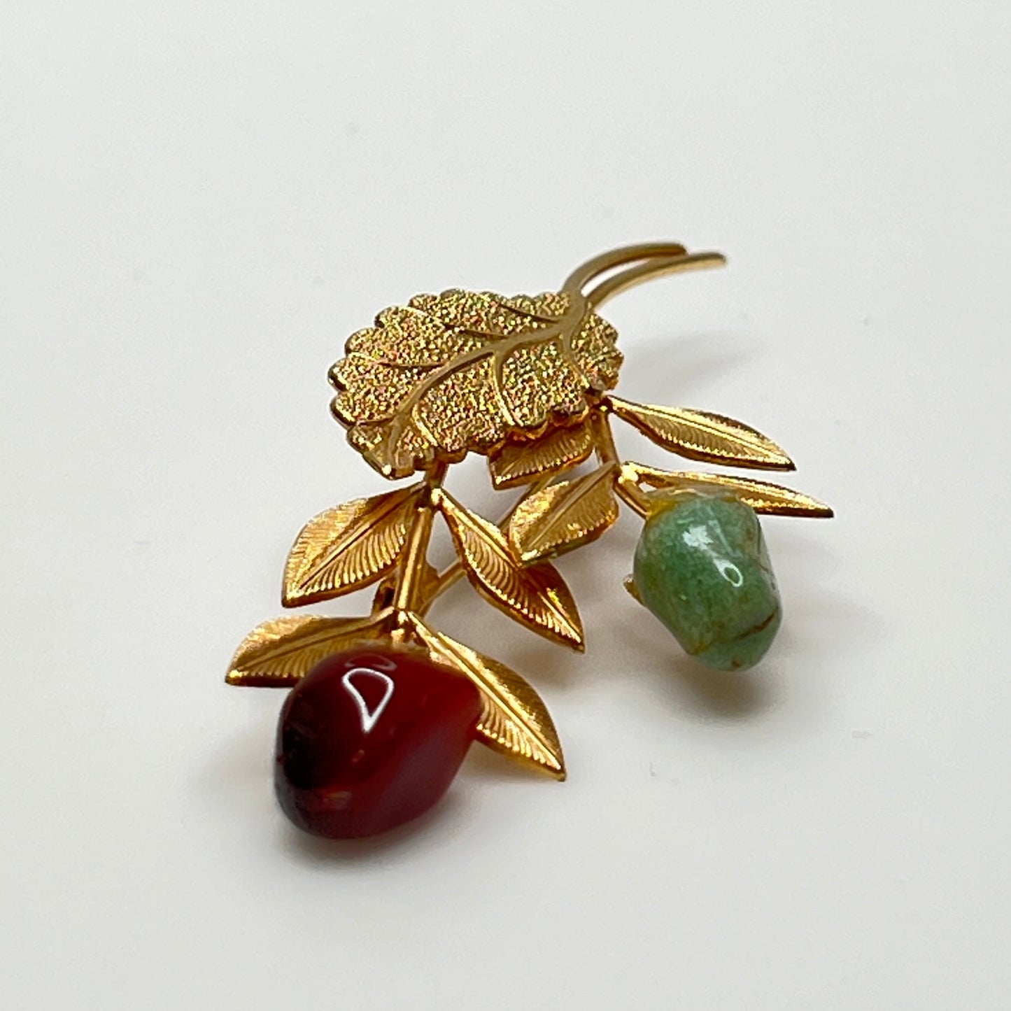 Close-up of jade cabochon rose bud floral brooch with textured gold leaves